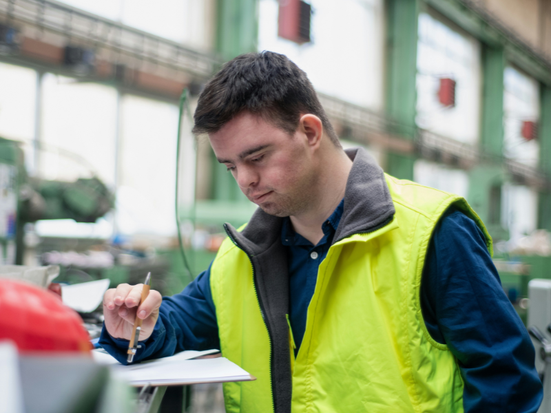 A imagem é um retrato de um trabalhador em um ambiente industrial, focando no tema de inclusão e diversidade no local de trabalho.