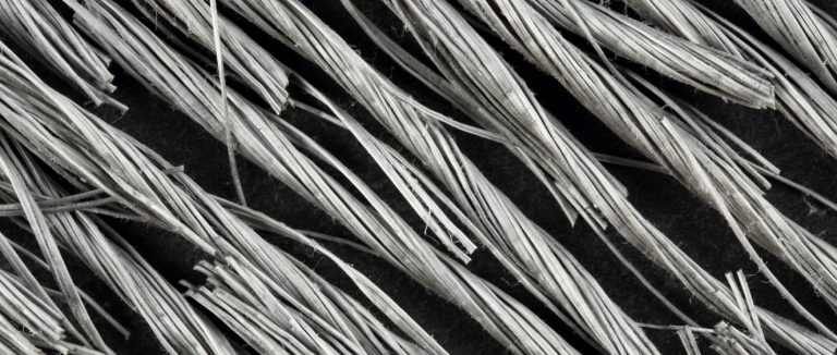 Vista em close extremo, de cima para baixo, de feixes de macrofibras de polipropileno cinza torcidas para reforço de concreto sobre fundo de pedra preta.