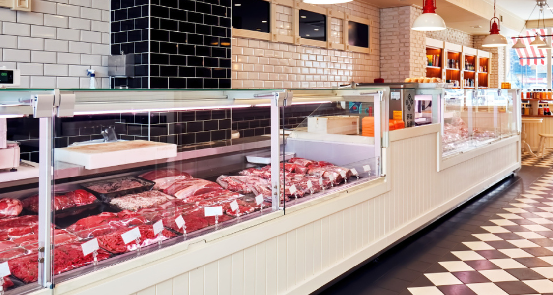 A imagem mostra o interior bem iluminado e moderno de um açougue de varejo ou uma seção de carnes gourmet.