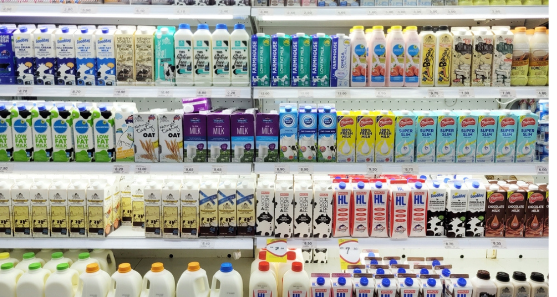 A imagem mostra uma prateleira de supermercado bem organizada, repleta de diferentes tipos de leites e bebidas vegetais refrigeradas. Os produtos estão distribuídos em várias fileiras horizontais e agrupados por marca ou tipo.