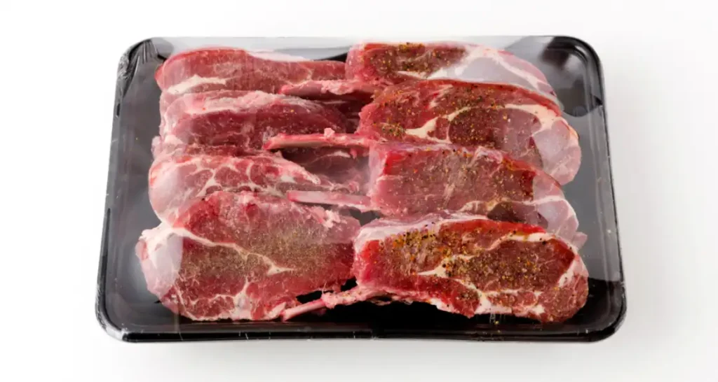 Cortes de carne bovina com tempero, prontos para preparo, apresentados sobre uma bandeja preta de uso culinário.