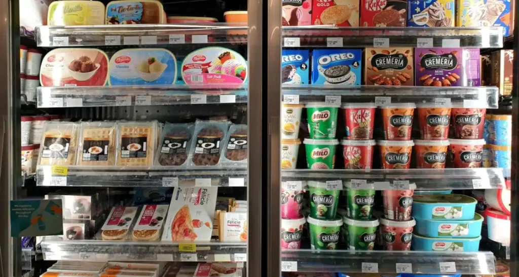 Refrigerador com uma variedade de produtos de sorvete e sobremesas Cremeria e Oreo em uma loja de conveniência, incluindo potes, barras e embalagens de diferentes sabores.