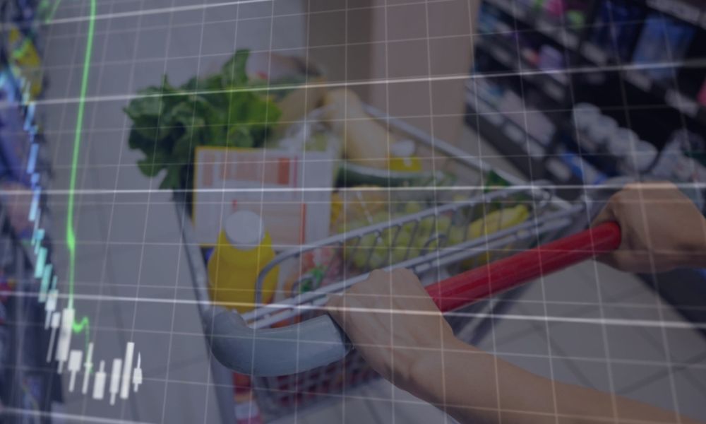 Vista superior de uma pessoa empurrando um carrinho de supermercado cheio de compras, com uma sobreposição gráfica de grade e um gráfico de vela (candlestick) verde subindo, sugerindo dados econômicos, inflação ou análise de consumo.