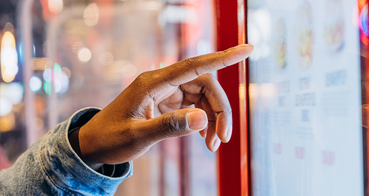 Totem de autoatendimento: Mão de um homem negro mexendo em uma espécie de tela grande de touchscreen