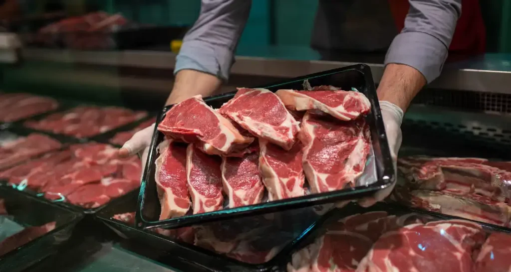 Homem apresentando cortes de carne bovina fresca em uma loja de açougue.