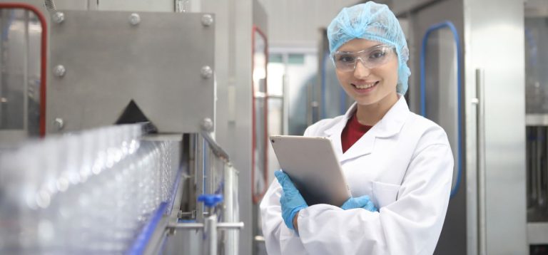 profissional com EPIs na indústria de alimentos sorrindo segurando prancheta