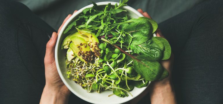 Uma tigela cheia de vegetais frescos, incluindo folhas verdes, brotos e fatias de abacate, exemplificando uma alimentação saudável.