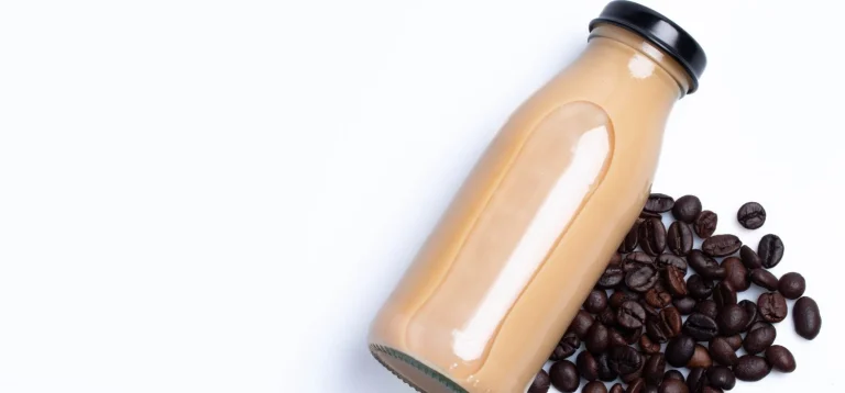 Garrafa de café gelado e grãos de café frescos em um fundo claro.