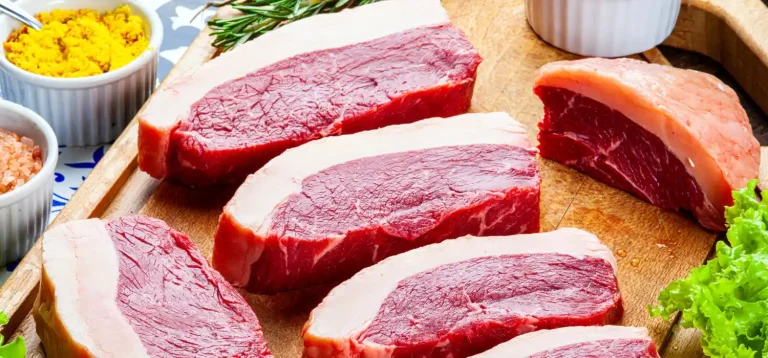 Cortes de carne bovina em uma tábua de madeira, acompanhados de temperos variados como sal e mostarda.