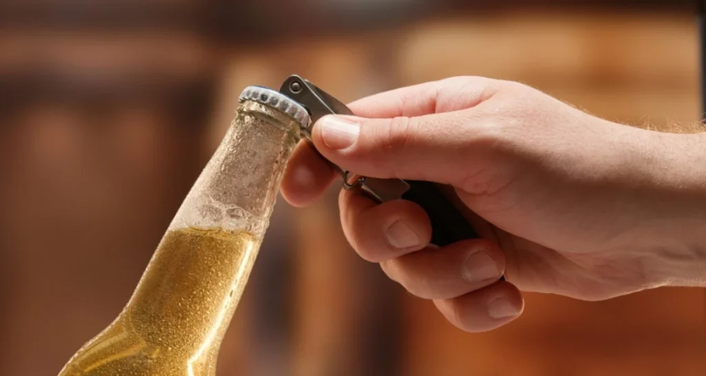 Mão segurando um abridor de garrafa, prestes a abrir uma garrafa de cerveja.