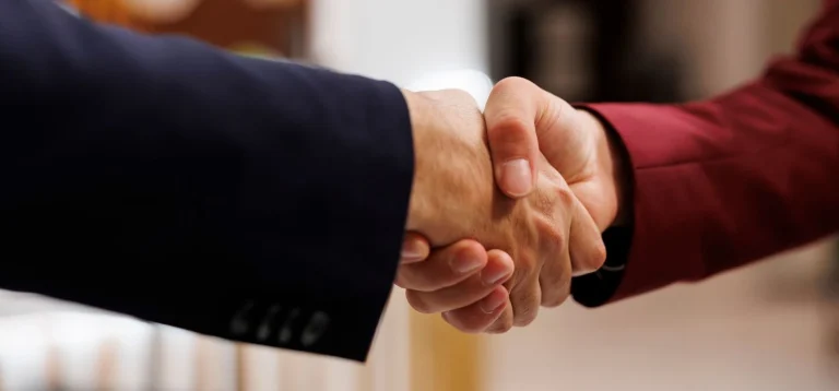 Duas pessoas realizando um aperto de mãos, simbolizando um acordo ou parceria em um ambiente profissional.