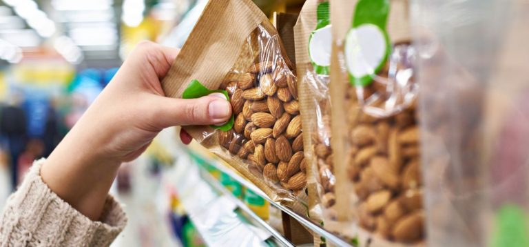 Mão segurando pacote de amêndoas em prateleira de mercado, destacando a variedade de opções saudáveis disponíveis para os consumidores.