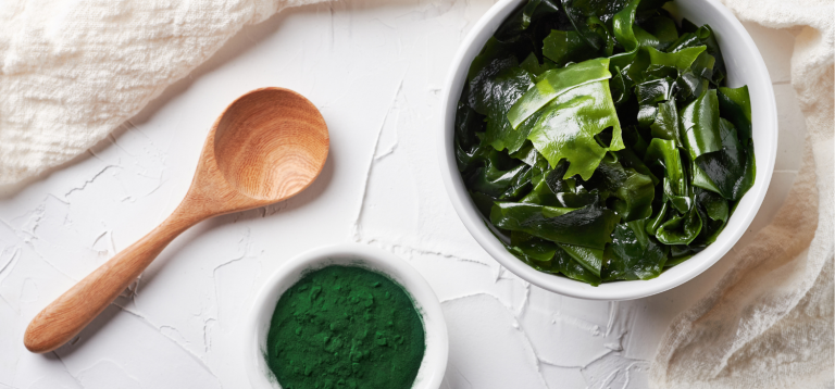 Imagem de alga marinha com uma colher de madeira e um recipiente com pó verde.