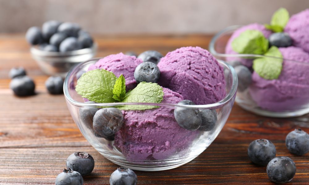 Bolas de sorvete de mirtilo (blueberry) servidas em taças de vidro com frutas frescas e hortelã.
