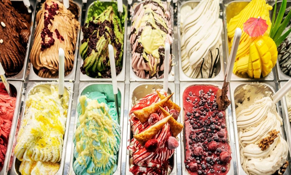 Vitrine colorida de gelateria com várias cubas de sorvete artesanal decoradas.