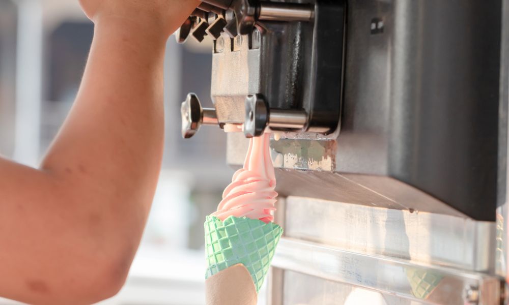 Máquina servindo sorvete expresso (soft serve) rosa em uma casquinha verde.
