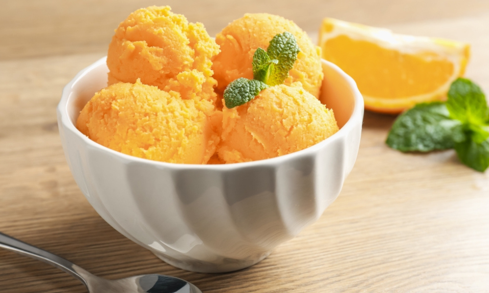 Taça branca com bolas de sorvete ou sorbet de laranja decorada com folhas de hortelã.