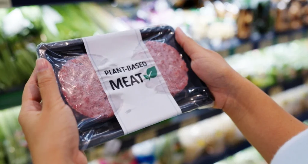 Pessoa segurando embalagem de carne vegetal à venda em supermercado, representando uma opção de carne à base de plantas para consumo consciente e sustentável.