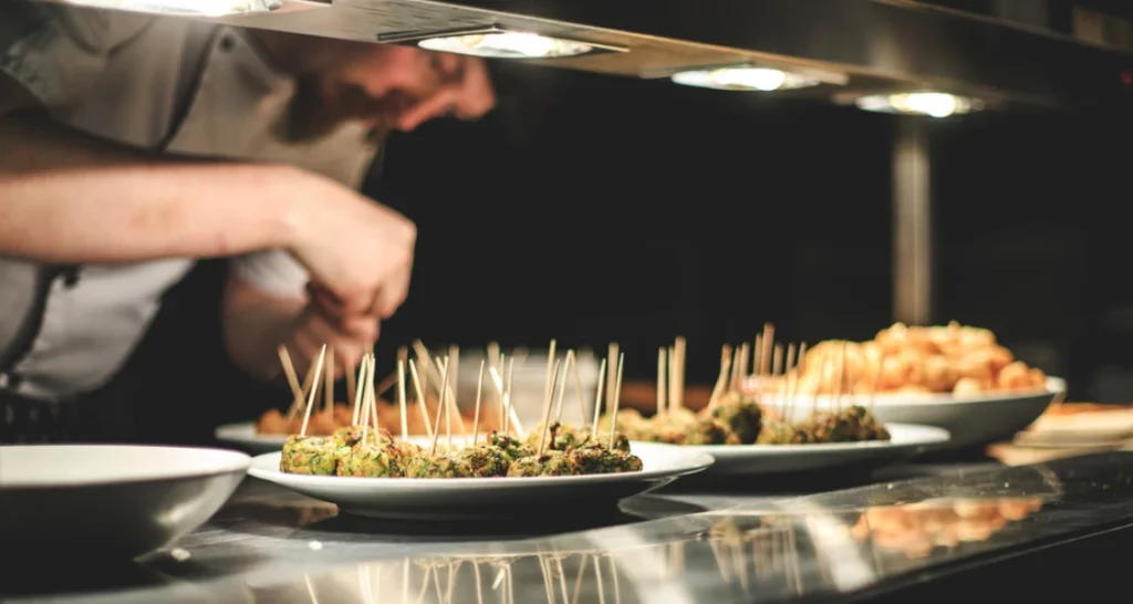 Chef preparando pratos de food service em uma estação de cozinha profissional, com foco em pratos elaborados e apresentação sofisticada para clientes.