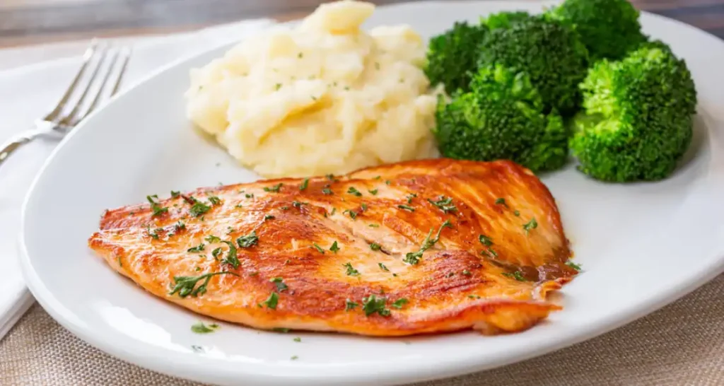 Filé de salmão grelhado com purê de batatas e brócolis frescos servido em prato branco.