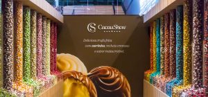 Exposição de diversas trufas artesanais de sabores variados na loja CacauShow, com destaque para trufas cremosas e coloridas.