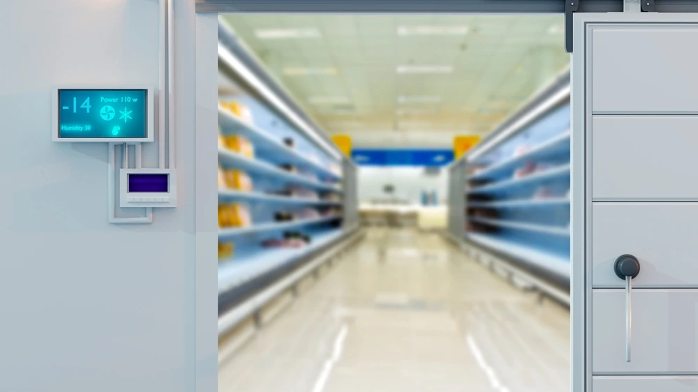 Geleira de supermercado com prateleiras vazias e sistema de controle de temperatura na parede ao lado.