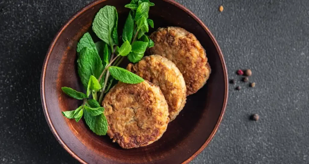 Três hambúrgueres artesanais com pão crocante, queijo derretido, alface e tomate, servidos em um prato preto.