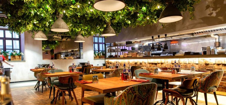 Restaurante elegante com decoração natural, incluindo teto com folhagem verde, iluminação aconchegante e ambiente sofisticado, ideal para refeições especiais. Imagem destaca a iluminação para restaurantes.