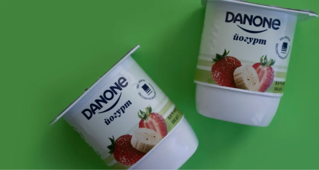 Iogurte Danone com sabor de morango e banana, embalagens dispostas sobre fundo verde, destaque para o produto natural e saudável.