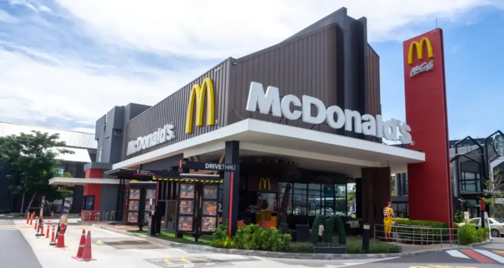 Imagem de uma unidade do McDonald's com fachada moderna, sinalização visível, área de atendimento drive-thru.