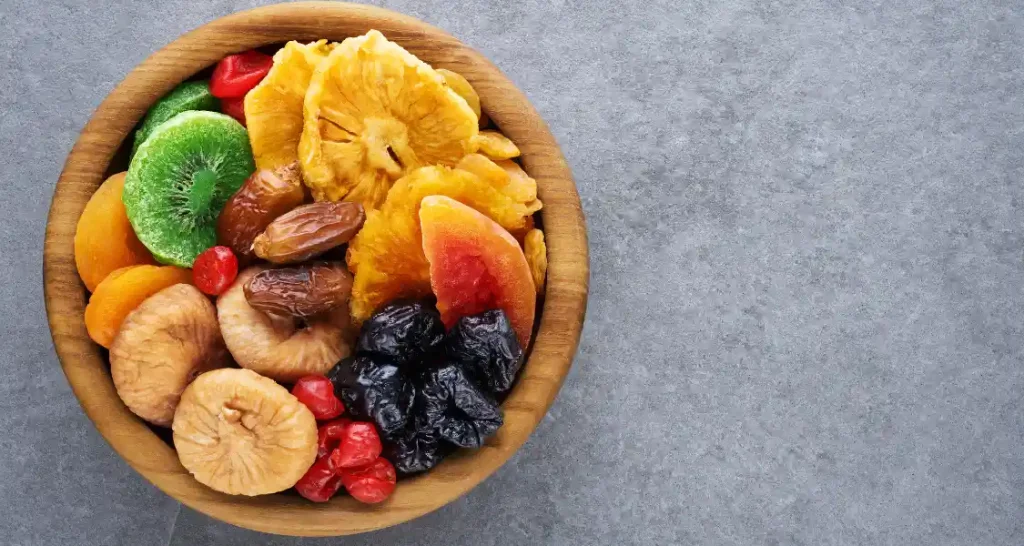 Mixture de frutas secas e frutas frescas em uma tigela de madeira, incluindo damascos, kiwi, uvas passas, figos, bananas, um pouco de polpa de melancia e outras frutas variadas.