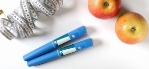Imagem de uma maçã, uma fita métrica, duas unidades de ozempic e um fundo branco, representando cuidados com a alimentação e saúde.