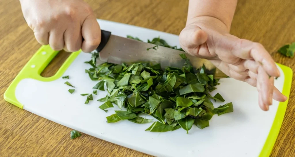 Pessoa cortando ora-pro-nóbis em uma tábua de cortar para preparar ingredientes frescos na cozinha.