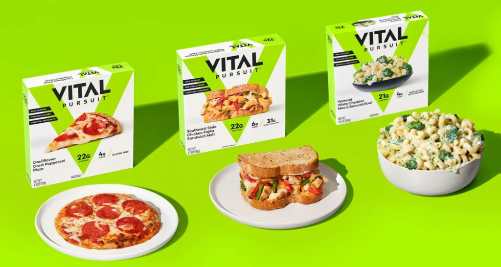 Variedade de produtos prontos para consumo da marca Vital Pursuit, incluindo pizza de pepperoni, sanduíche e macarrão com queijo, em fundo verde vibrante.