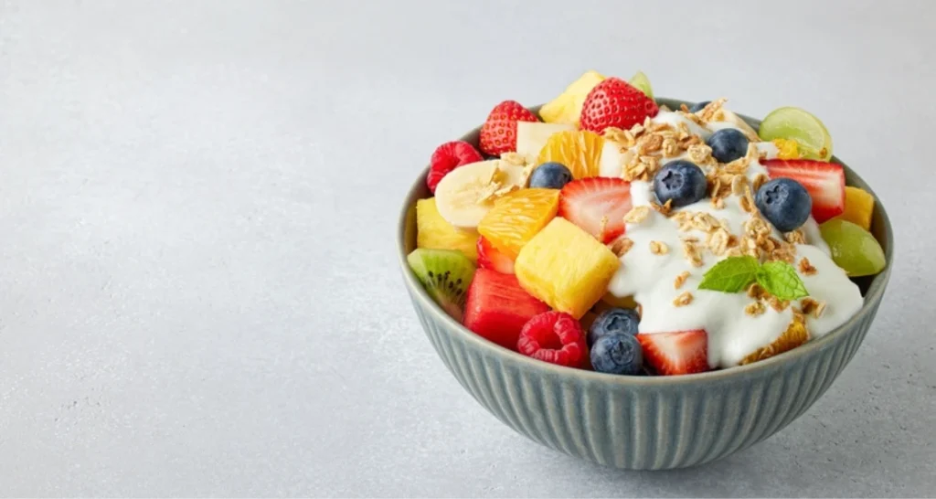 Tigela de açaí com frutas frescas, incluindo morangos, blueberries, kiwis, bananas e abacaxi, decorada com granola e hortelã.