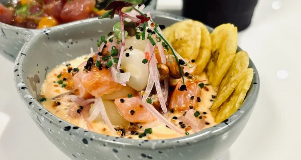 Salada de peixe com molho especial, decorada com cebola, sementes, cebolinha, batata chips e microverdes, servida em tigela de cerâmica.
