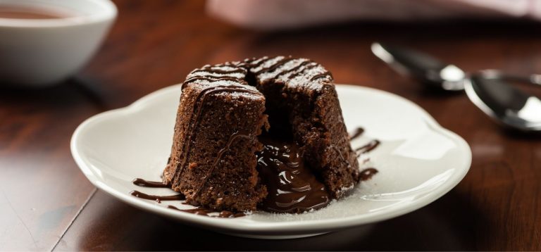 Imagem de um bolo de chocolate quente com recheio derretido, decorado com calda de chocolate, servido em um prato branco. Opção para sobremesas quentes com sorvete.
