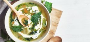 Sopa de ervas frescas com especiarias, acompanhada de folhas de hortelã e um toque de creme, opção saudável para tendências de cardápios.