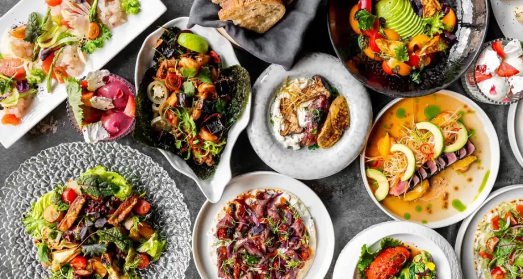 Variedade de pratos tradicionais asiáticos em uma mesa, incluindo sushi, sashimi, rolinhos primavera e acompanhamentos coloridos.