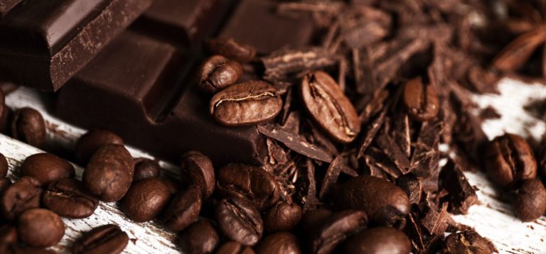 Imagem de grãos de café, pedaços de chocolate e castanhas dispostos sobre uma superfície de madeira. Imagem reflete sobre os alimentos afetados pelas mudanças climáticas.