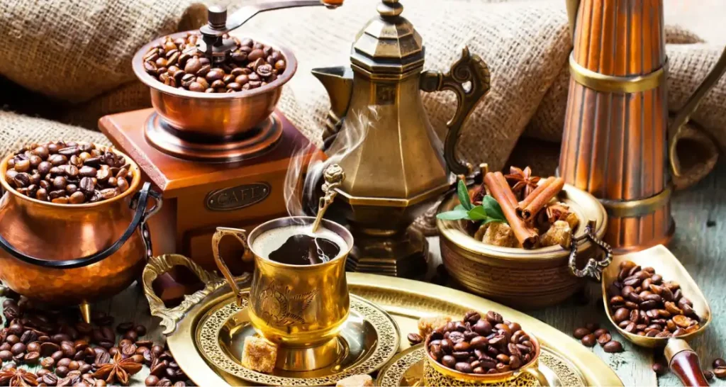 Imagem de café tipo arábica e utensílios de cobre em uma mesa de café, incluindo grãos de café, uma cafeteira antiga, e especiarias.