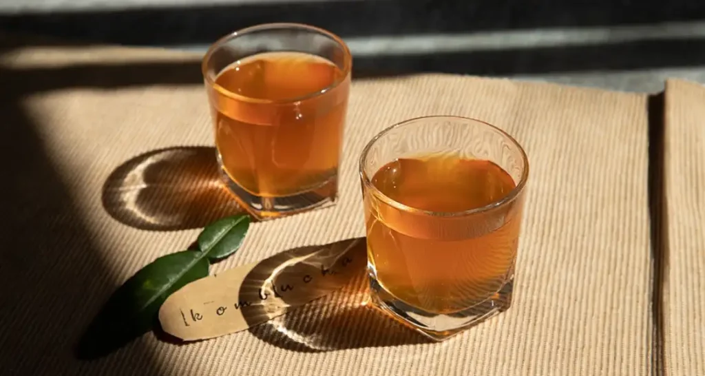 Dois copos de  kombucha sobre uma mesa de papel kraft, com efeitos de luz e sombra que destacam a transparência da bebida funcional.