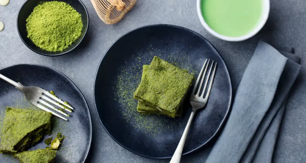 Doces de abacate com cobertura de matcha em pratos pretos, acompanhados de chá verde em xícara branca, ideal para quem busca receitas saudáveis e diferentes