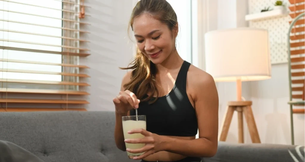 Mulher sorridente tomando uma bebida funcional em casa, ambiente acolhedor com luz natural. 