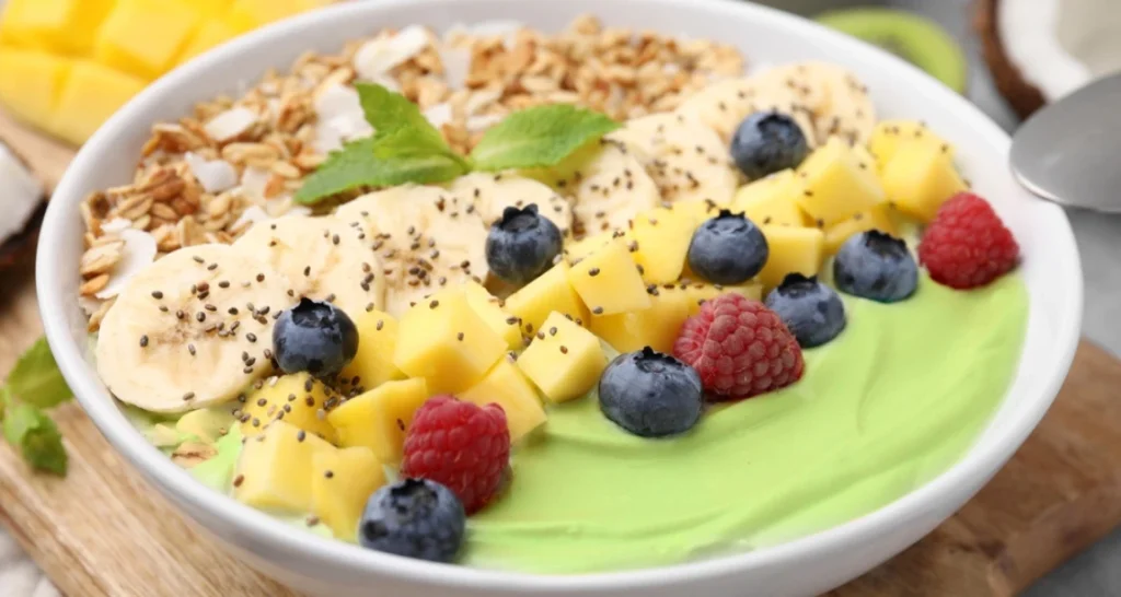 Vitamina com frutas frescas, como banana, manga, morango e amora e matcha, decorada com granola e hortelã, perfeita para um café da manhã saudável.
