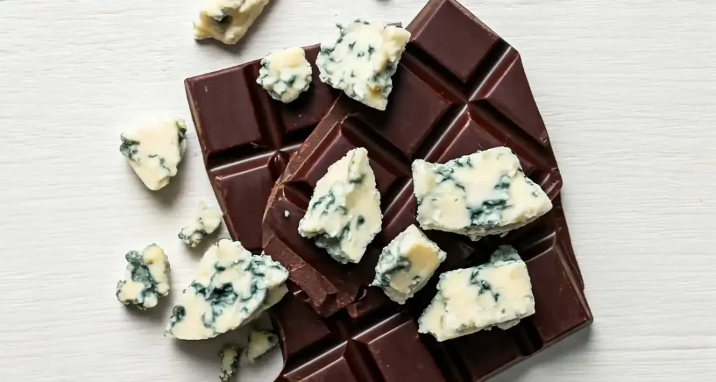 Barra de chocolate meio amargo com pedaços de queijo azul em fundo de madeira. 