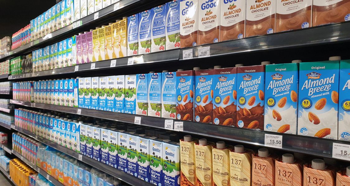 A imagem mostra uma prateleira de supermercado repleta de bebidas à base de plantas, organizadas lado a lado. As embalagens são coloridas e variadas, representando diferentes marcas e sabores.