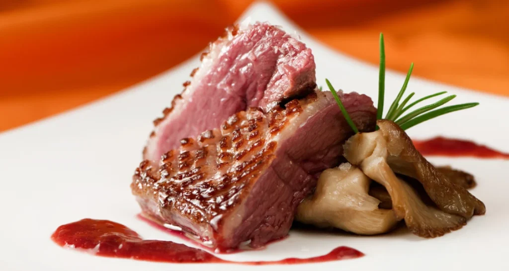 Prato com carne ao ponto, acompanhado de cogumelos e molho de vinho ao lado, servido em um prato branco com decoração de ervas.