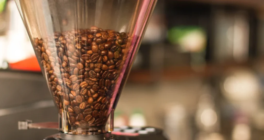 Grãos de café sendo moídos em um moedor profissional, destacando a preparação para a produção de café de alta qualidade.