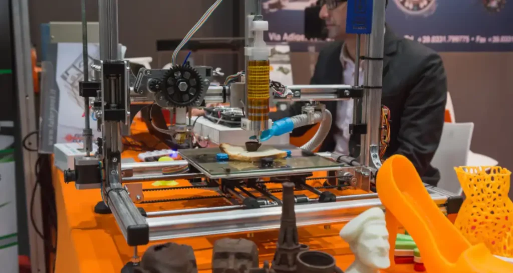 Impressora 3D em ação criando objetos de diferentes formatos, incluindo esculturas e peças de arte, em evento de tecnologia e inovação.